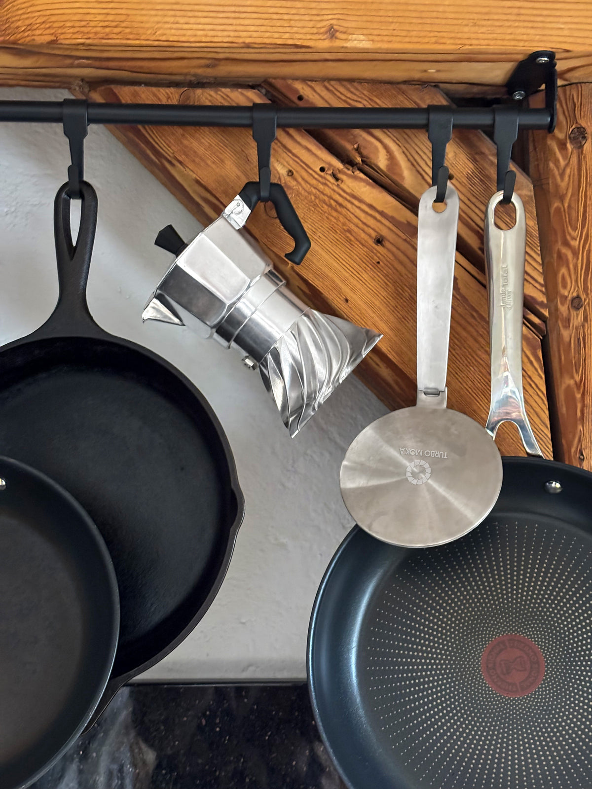 Turbo Moka and the stainless steel induction adapter disk hanging from a kitchen rail beside cast iron pans