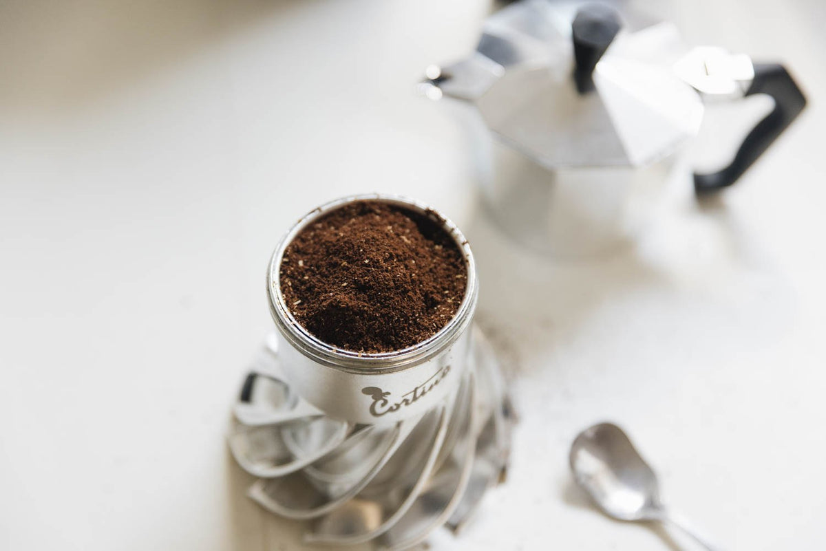 Turbo Moka Cortina Edition boiler filled with freshly ground coffee, spoon and moka top in the background
