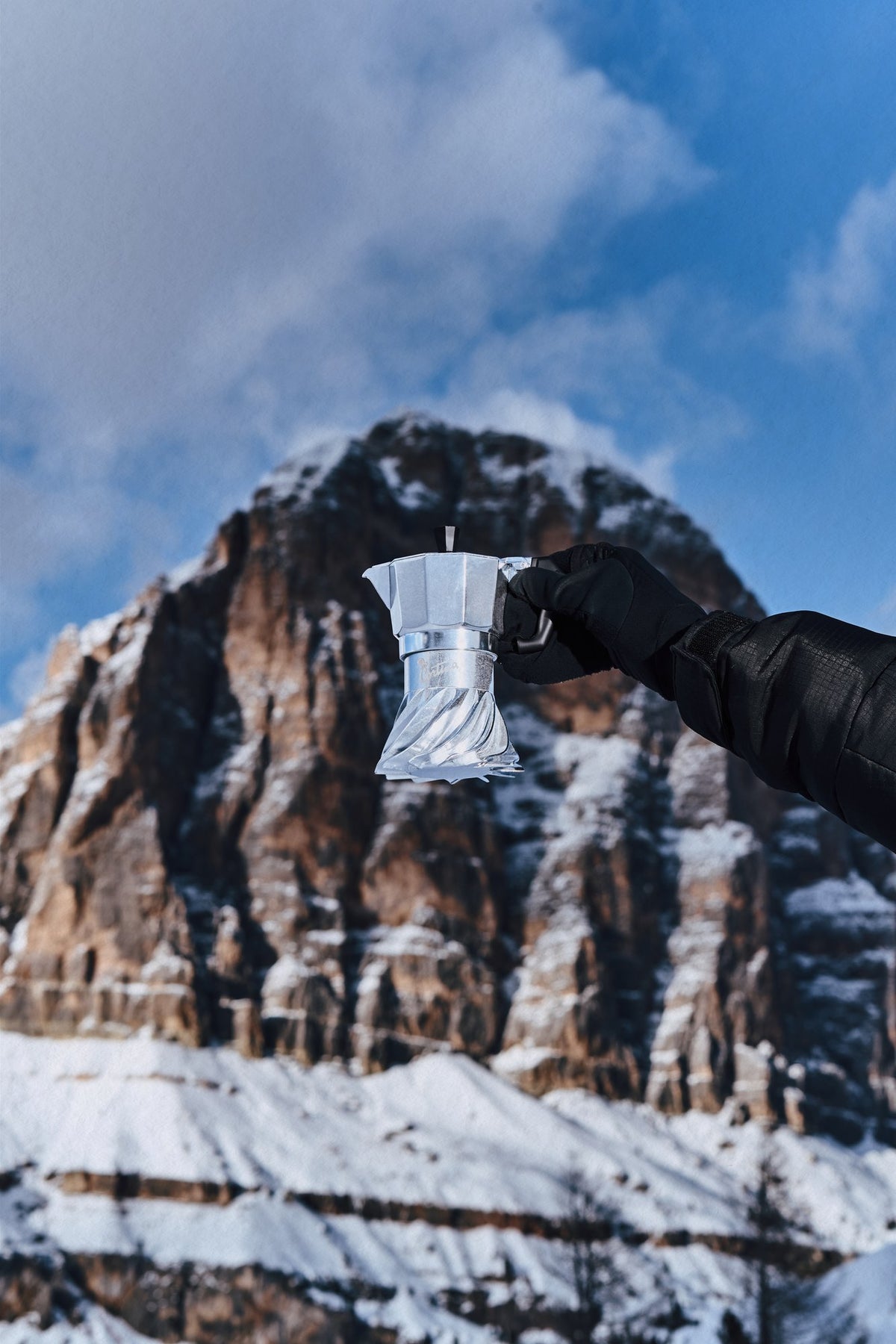 Gloved hand holding the Turbo Moka Cortina Edition in front of the Dolomite peaks above Cortina d'Ampezzo