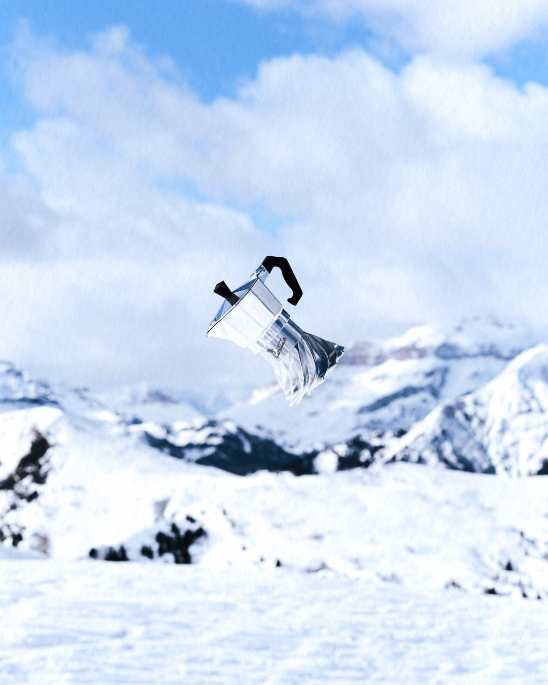Turbo Moka Cortina Edition suspended in mid-air against a blue sky above the snow-covered Dolomites