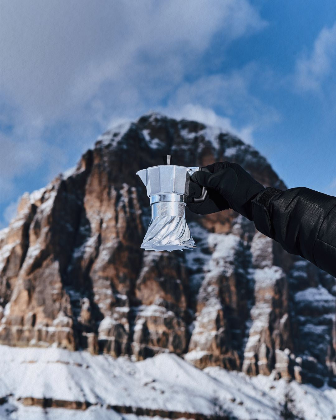 Gloved hand holding the Turbo Moka Cortina Edition in front of a snow-covered Dolomite peak above Cortina d'Ampezzo