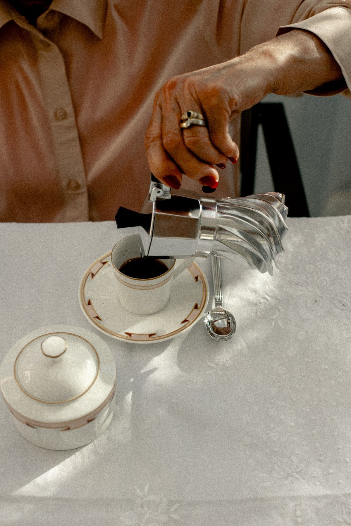Pouring coffee from the Turbo Moka into a porcelain cup on a linen-covered Italian breakfast table