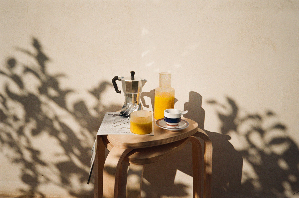 Turbo Moka on a wooden table with orange juice and a blue-and-white cup, leaf shadows on the beige wall behind